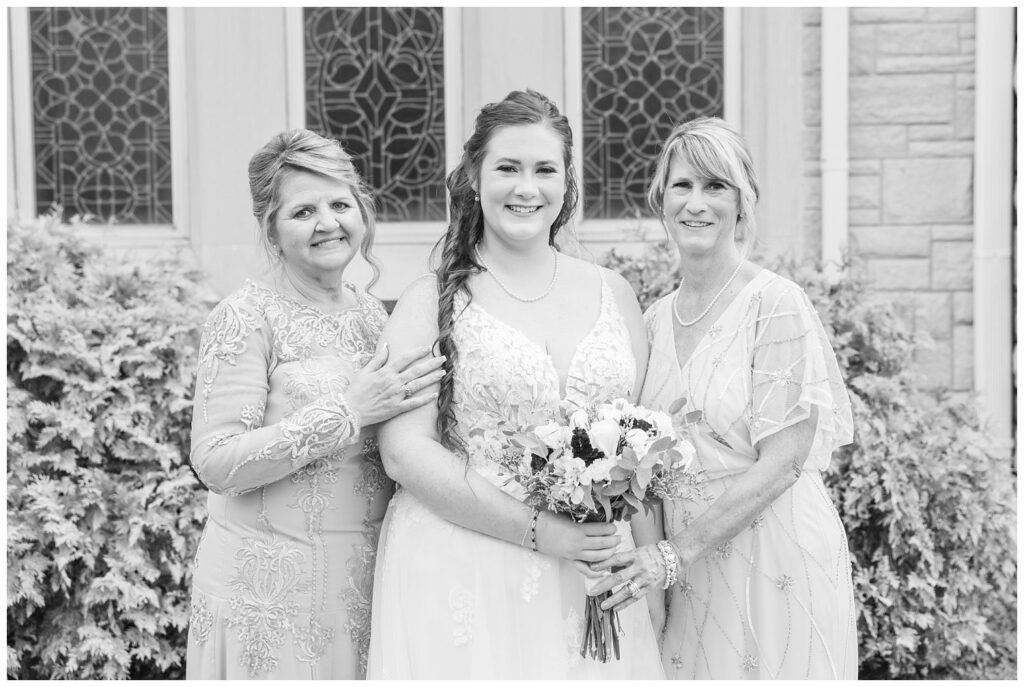 bride posing with her mom and groom's mom outside the church