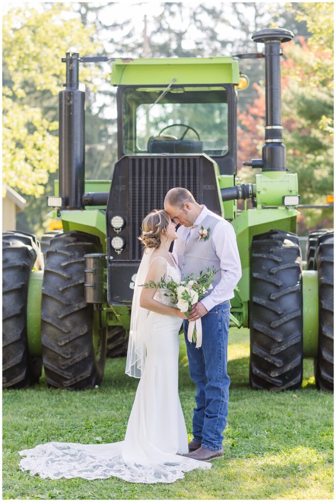 wedding couple touching foreheads in front of a large green tractor