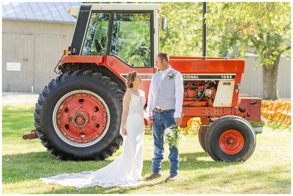 groom holding the bride's bouquet in front of a large red tractor