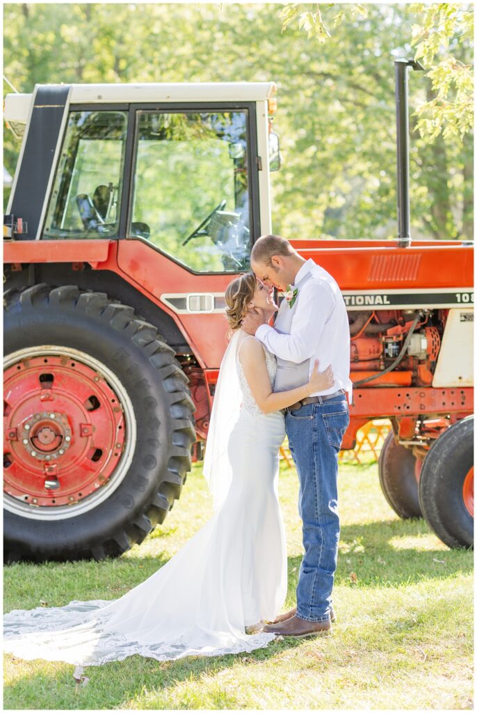 bride and groom touching noses in front of a large red tractor in Ohio