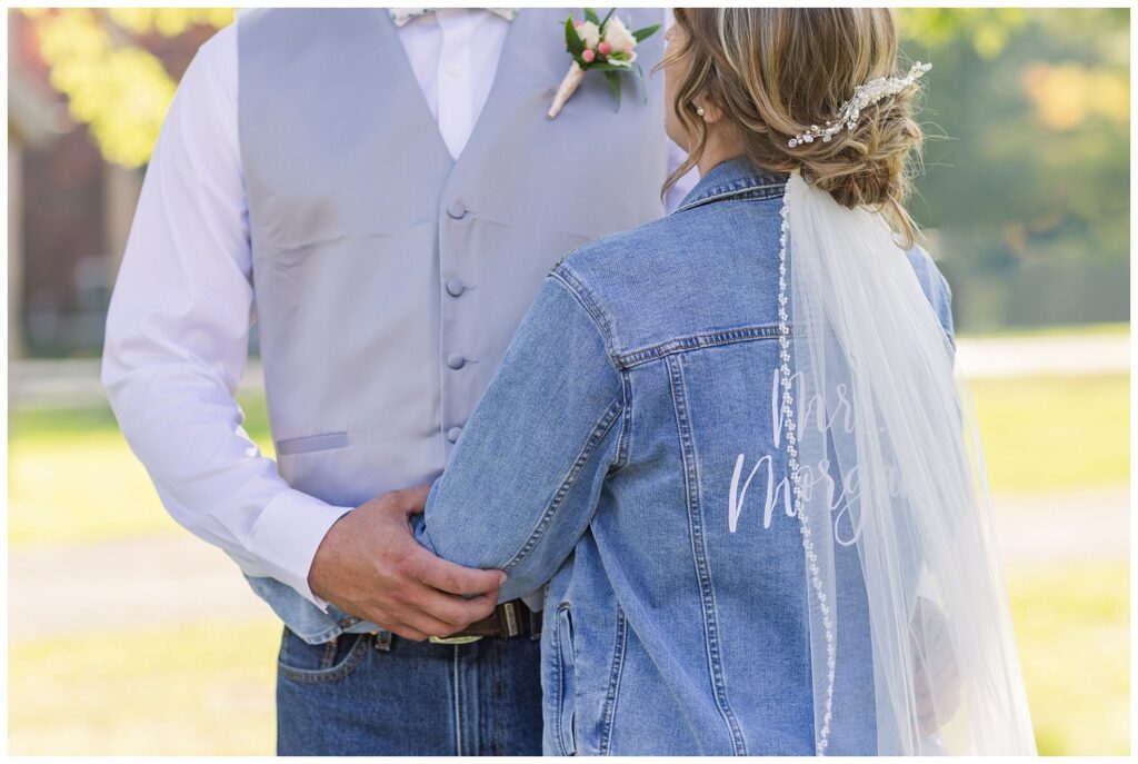 bride wearing a jean jacket and her veil posing with the groom