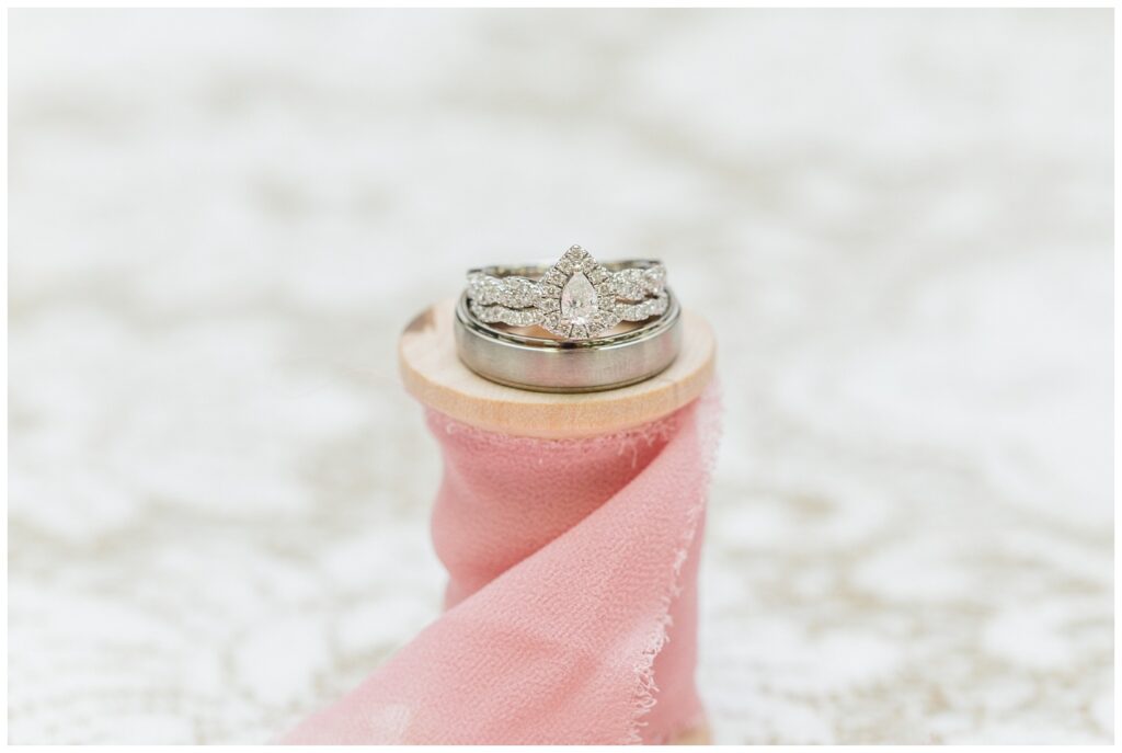 white hold wedding rings sitting on top of a spool of pink ribbon