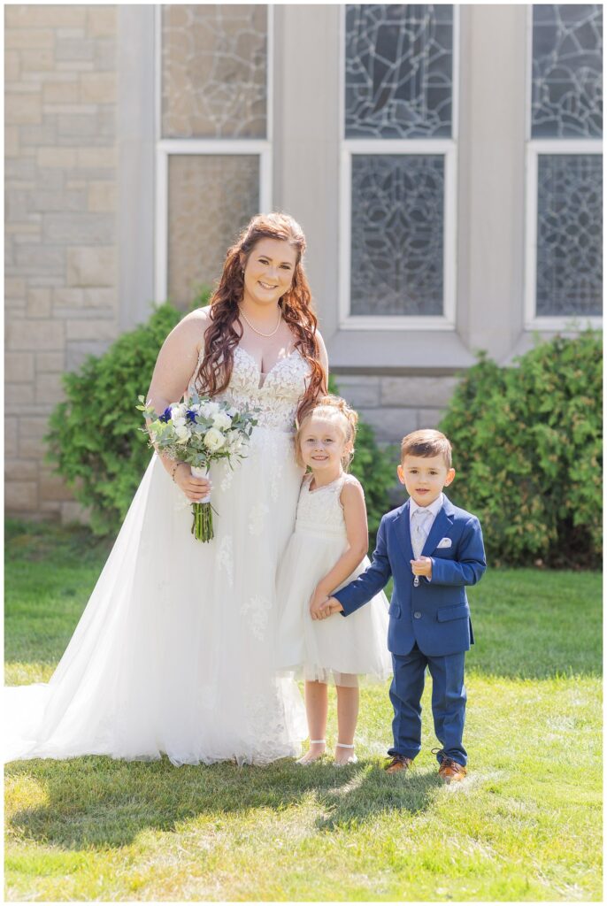 bride posing with flower girl and ring bearer outside the church for fall wedding