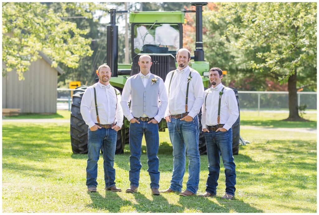 groomsmen posing in front of a large green tractor at Huron County wedding
