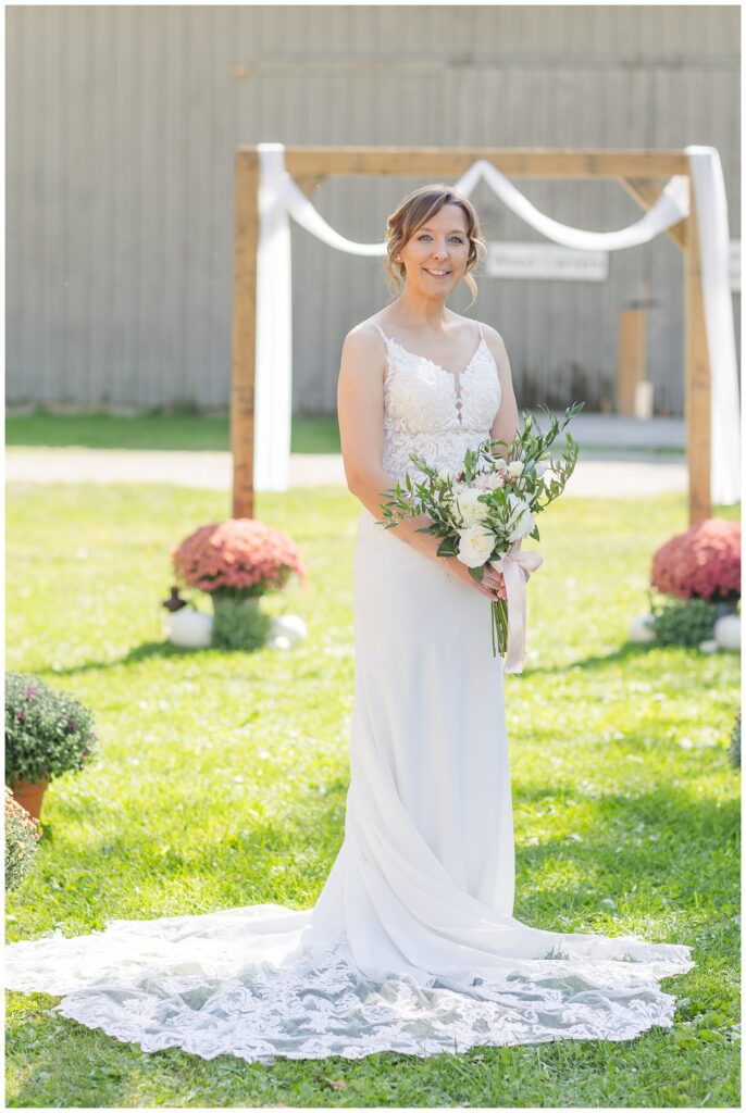 a fall bride holding a bouquet and posing in front of a wooden arch 