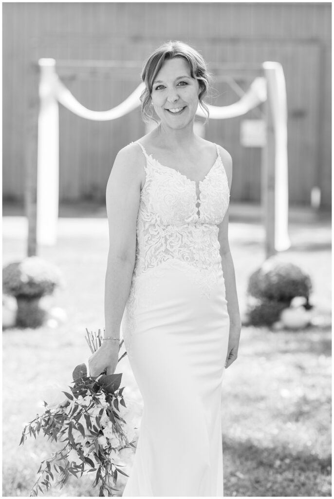 a fall bride holding a bouquet and posing in front of a wooden arch 