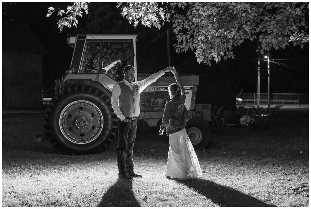 night time portraits outside next to tractors with the groom twirling bride in northwest Ohio
