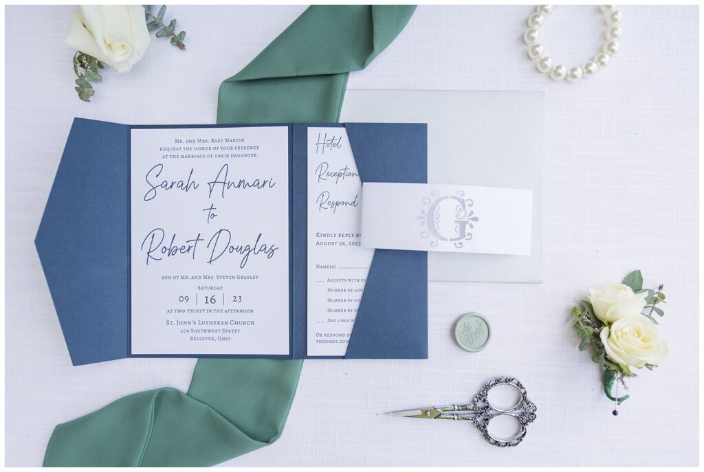 blue and white invitation suite sitting on a white backdrop with jewelry