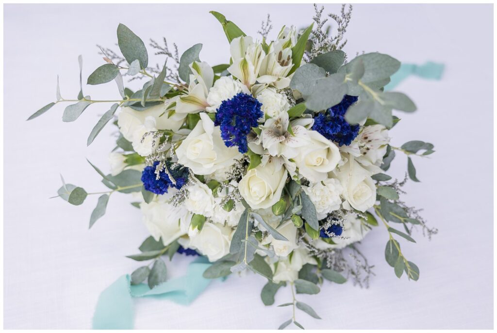 bride's blue and ivory wedding bouquet sitting on a white mat with green ribbon