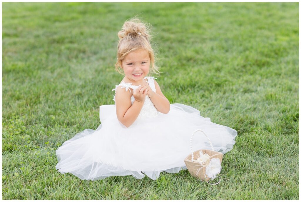 bride and groom's daughter sitting on the ground with her flower basket