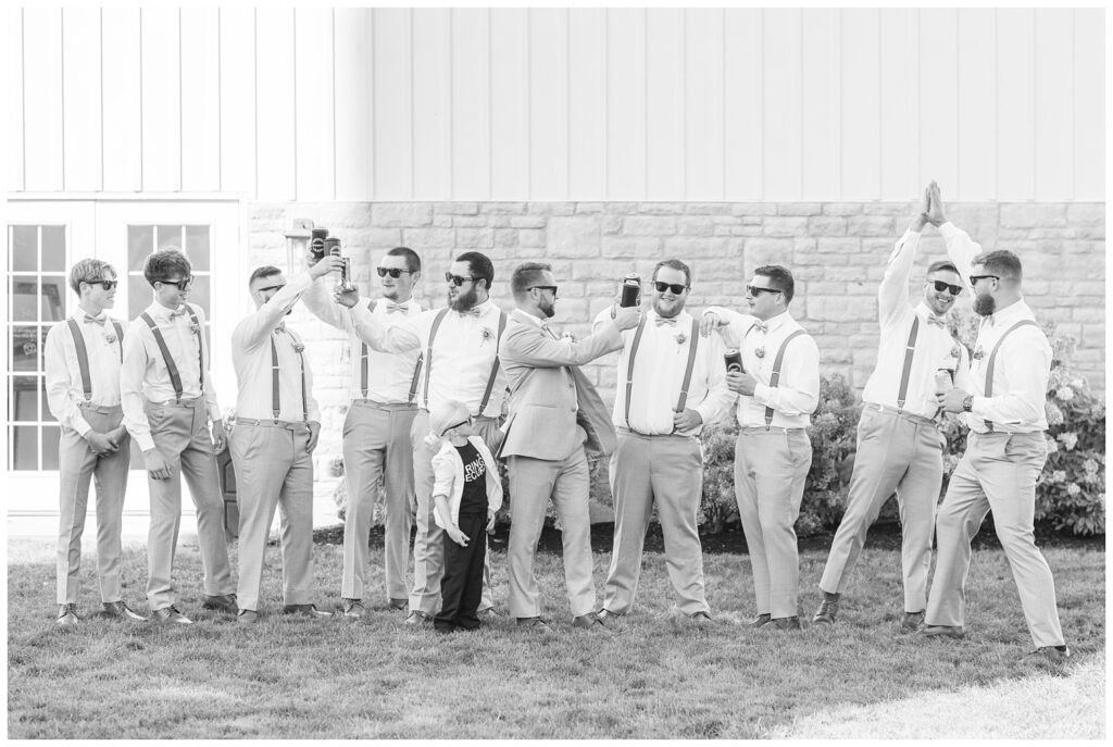 groomsmen toasting drinks and wearing sunglasses in front a stone wedding venue in northwest Ohio