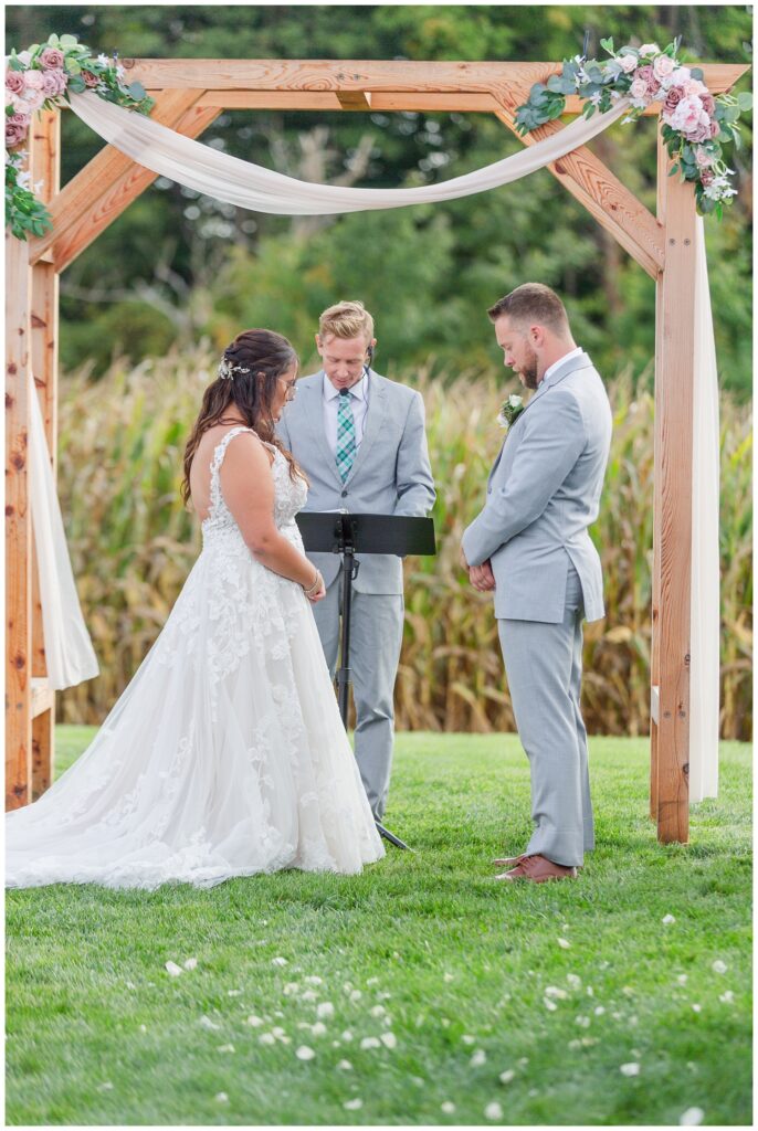 wedding couple bowing their heads in prayer during outdoor fall ceremony