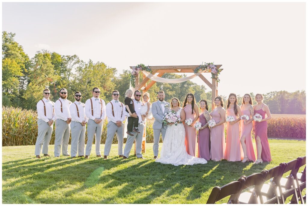 full wedding party posing at the ceremony arch at Arlington Acres venue