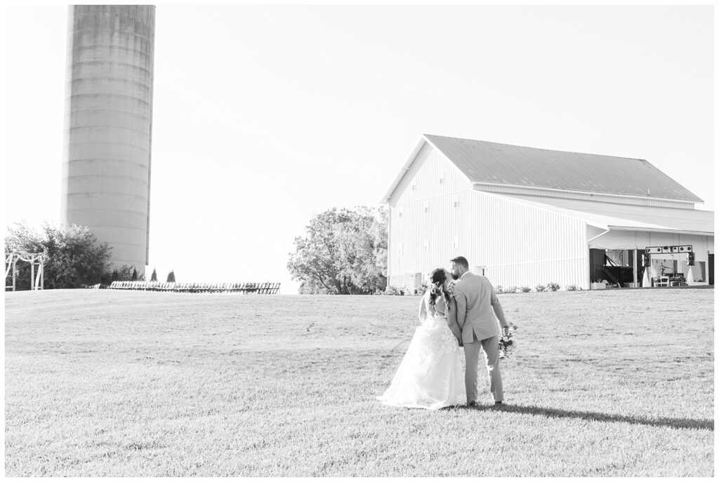 bride and groom share kiss as they walk towards the white barn reception