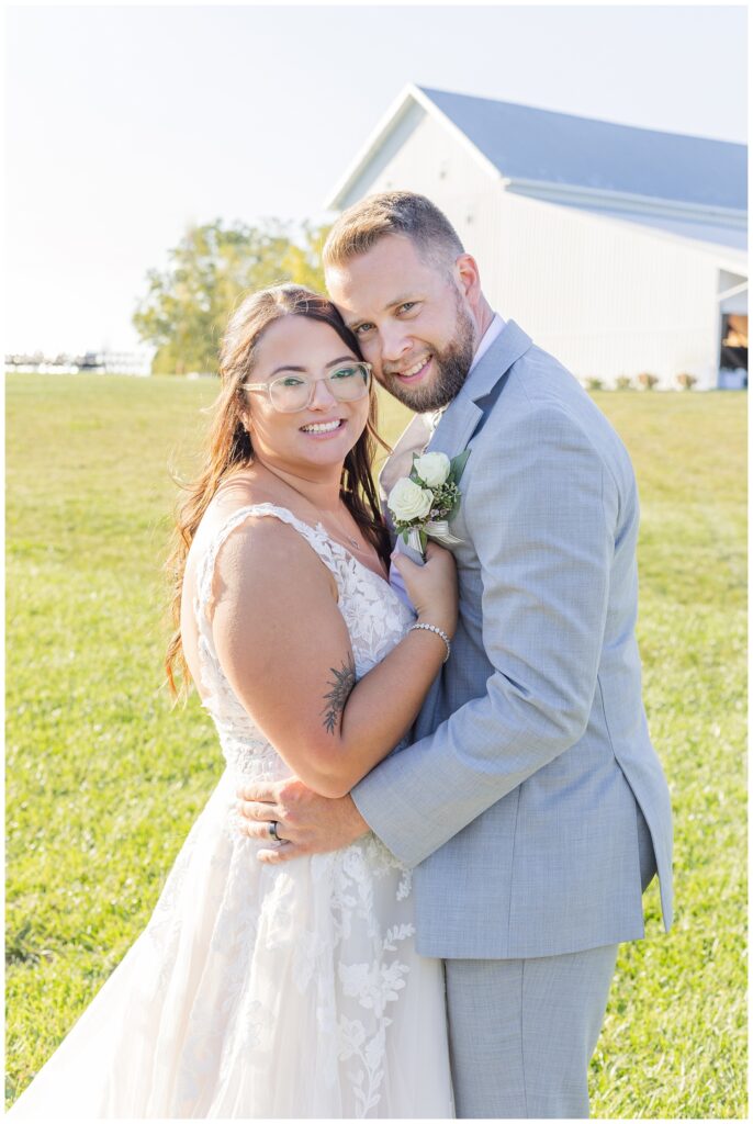 bride and groom holding each other in front of white barn venue in northwest Ohio