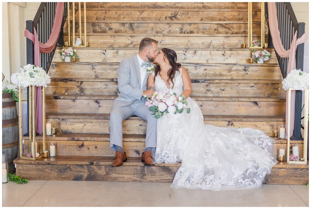 bride and groom sitting on wooden stairs and share kiss at reception venue