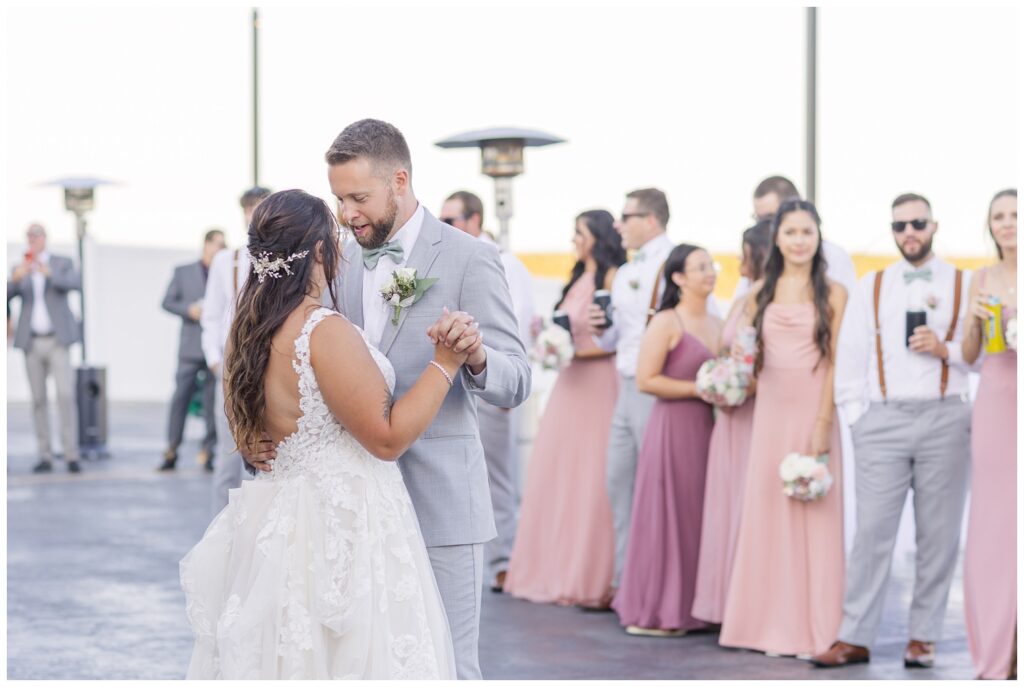 bride and groom have first dance outside during reception while bridal party stands near