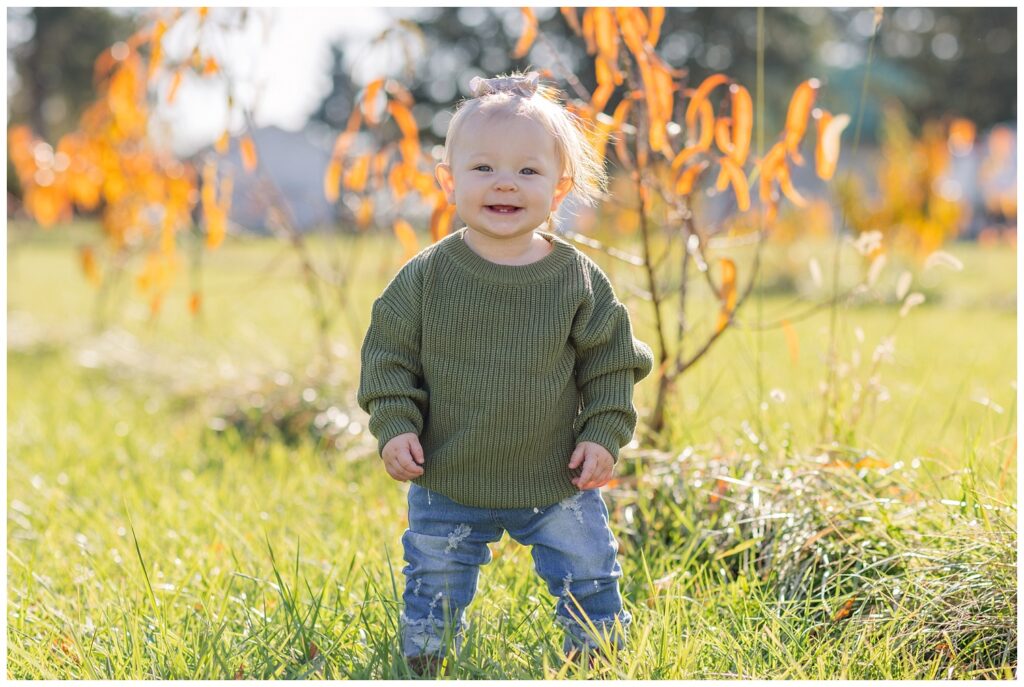 1 year old wearing a green sweater, jeans, and boots outside at Ohio portrait session