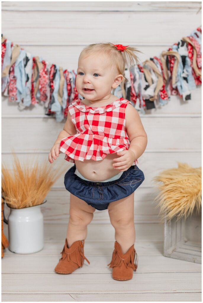 little girl wearing a red gingham and cowboy boot outfit at studio milestone session