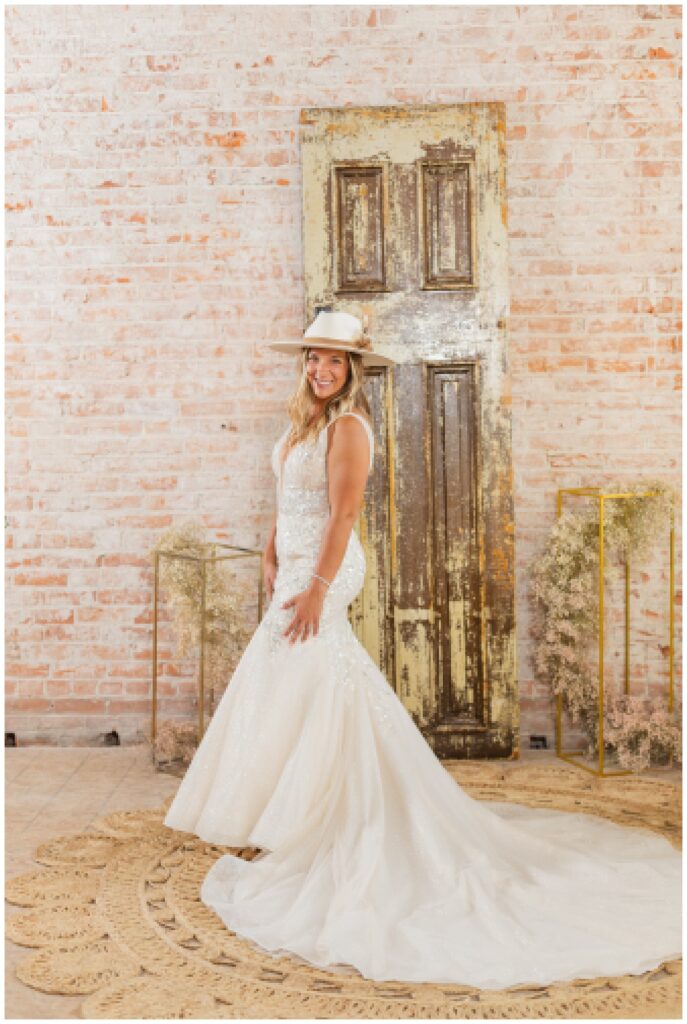 bride smiling and posing while wearing a ivory colored wedding dress and cowboy hat