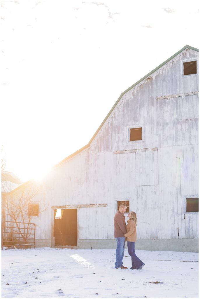 engaged couple smiling in front of a white barn at Fremont, Ohio farm