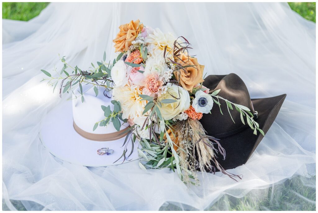 bride and groom's cowboy hats sitting on top of the bride's veil and flowers