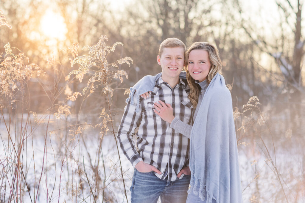 couple wrapped in a blue blanket standing in the snow 