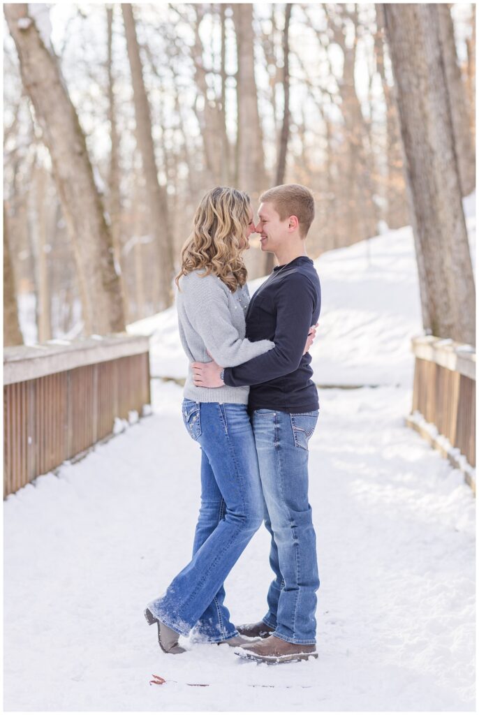 couple wearing jeans and hugging on a snow covered bridge in Ohio