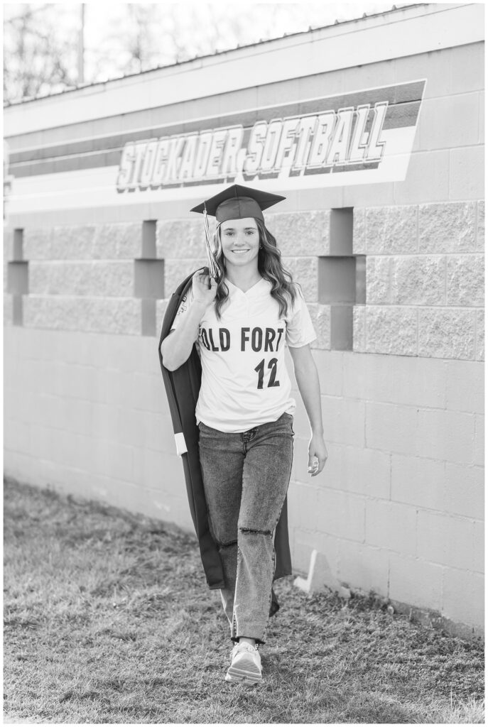 senior girl wearing a softball uniform and cap walking towards the photographer