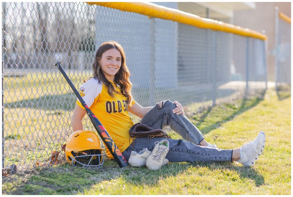 senior girl with baseball stuff leaning against a fence in Ohio