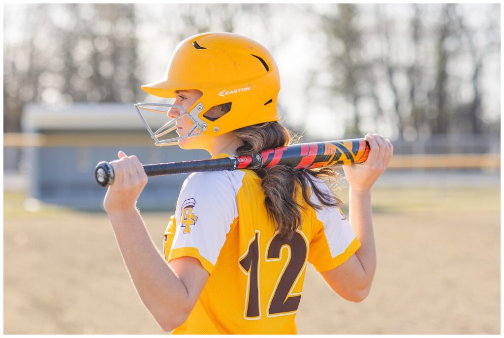 girl holding a bat behind her neck while wearing a helmet