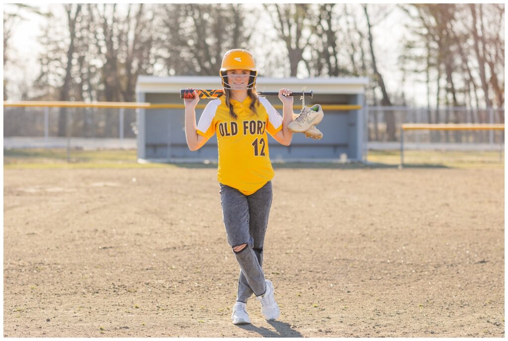senior girl posing on a ball field wearing her softball gear