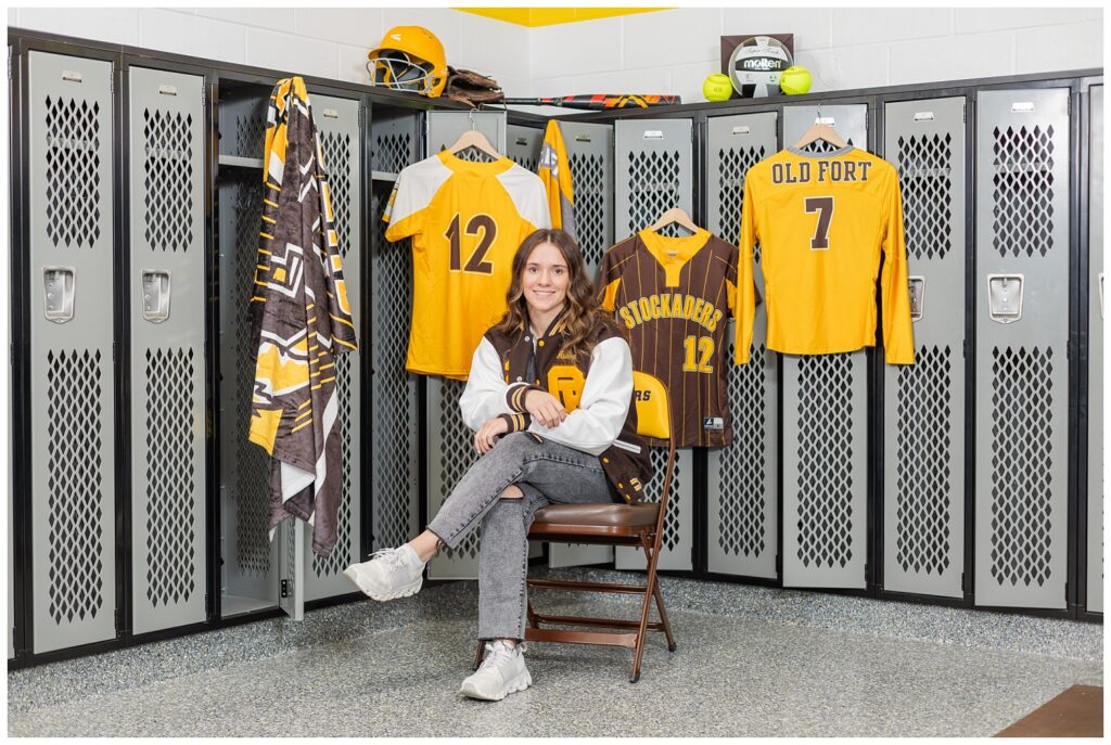 senior girl posing in the locker room with all of her uniform tops 