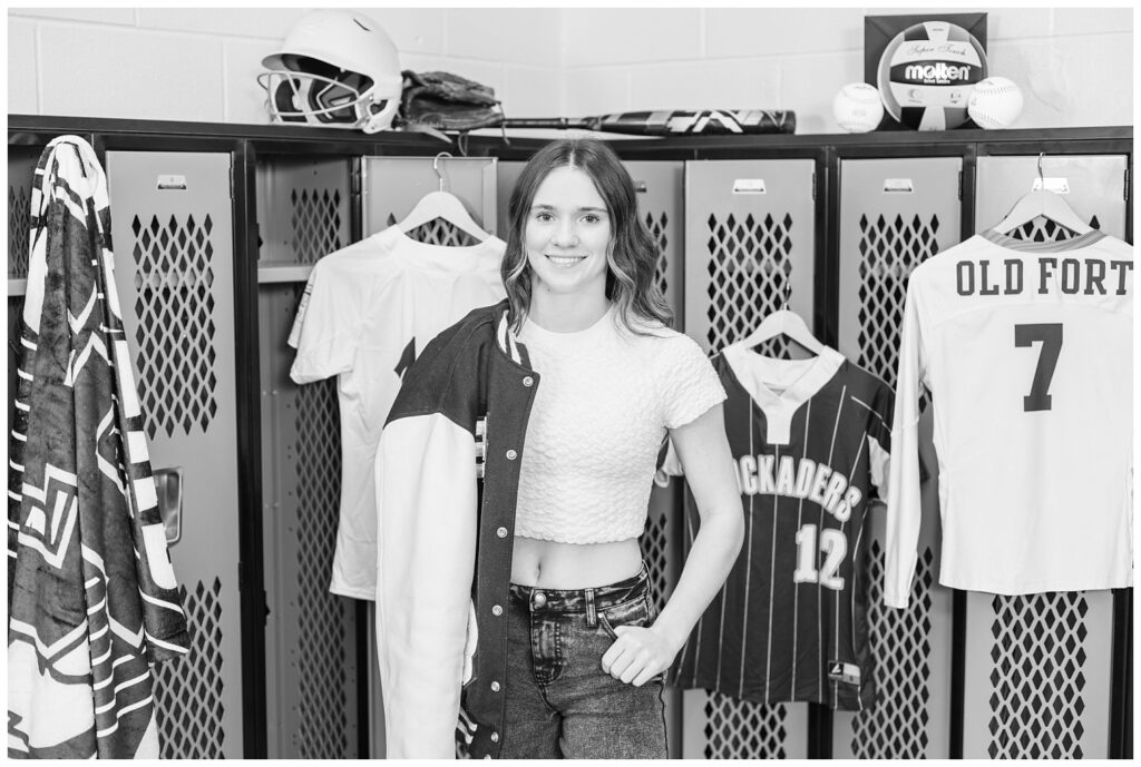 Old Fort high school senior posing with all of her sports uniforms in the locker room