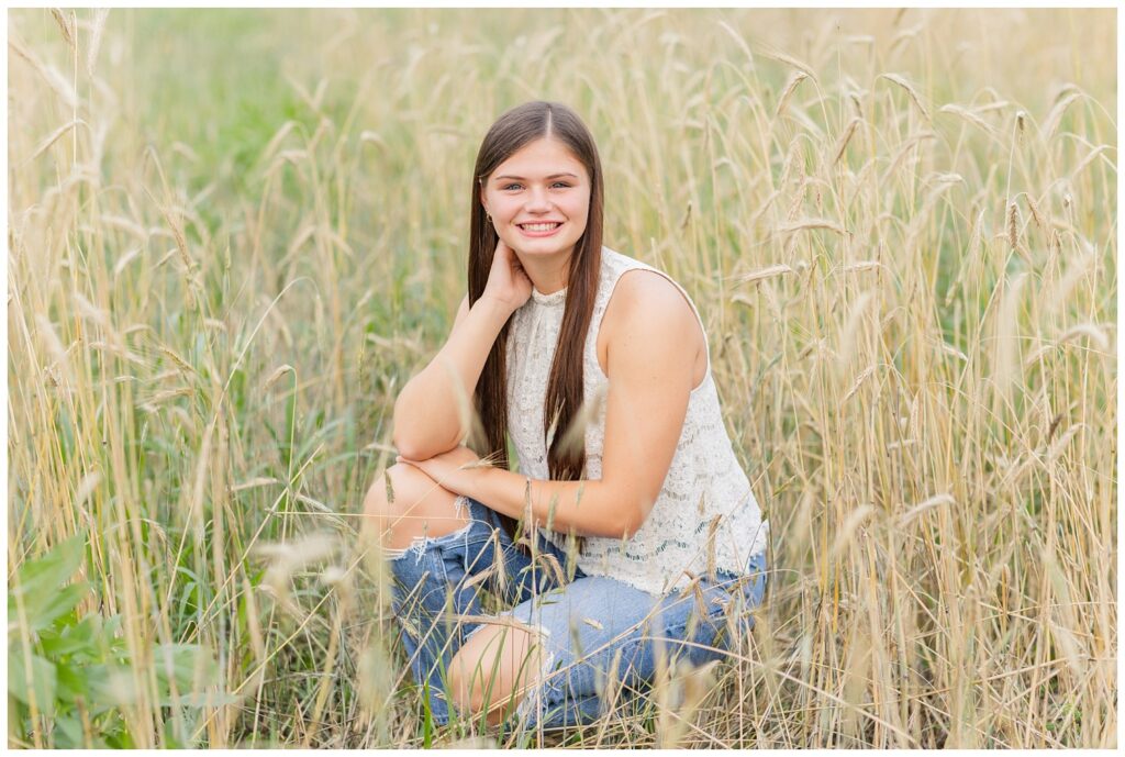 high school senior girl crouched down in a wheat field in Ohio