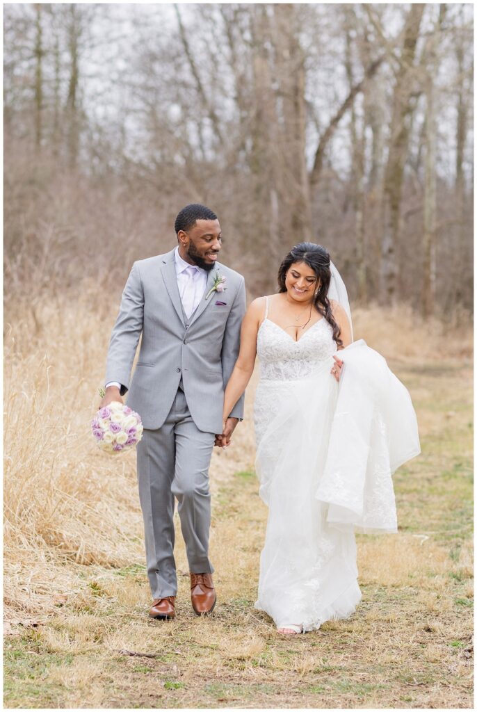 groom holding the bride's bouquet and walking with bride in field 