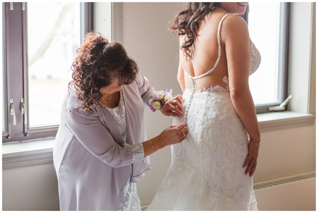 bride's mom adjusting the bride's dress in front of a window