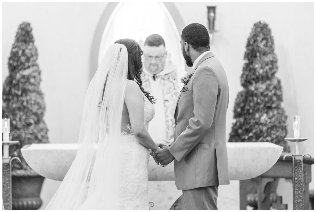wedding couple holding hands and looking at the pastor during Catholic church wedding