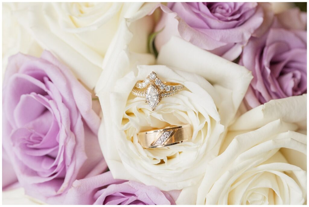 gold and diamond wedding rings sitting in a white and lavender rose bouquet
