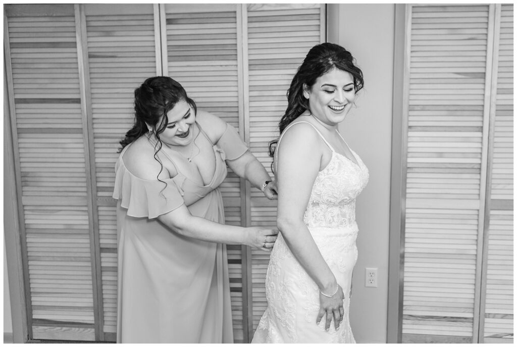 bridesmaid zipping up the back of the bride's dress in front of a closet