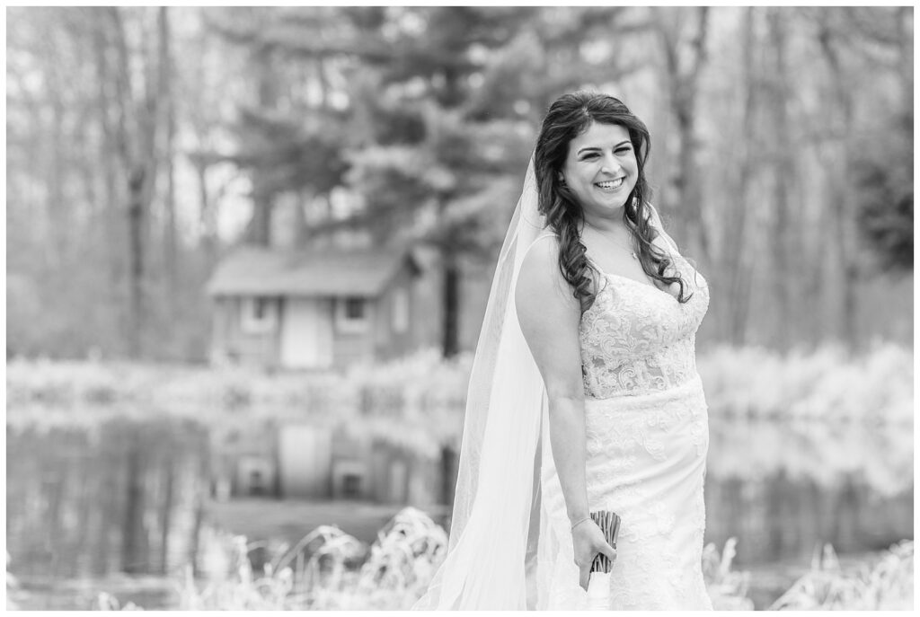 bride holding her bouquet to the side and posing in front of a pond outside 