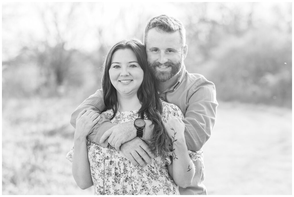 fiance hugging his girlfriend from behind while standing in a field