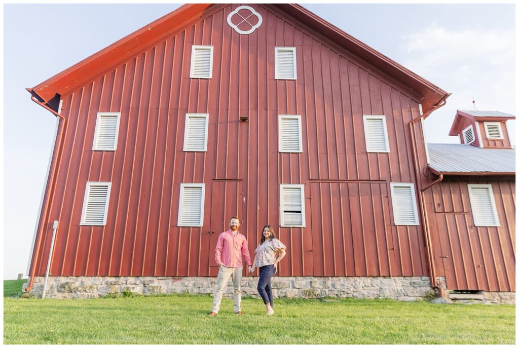 engaged couple posing in front of a red barn at Creek Bend Farm