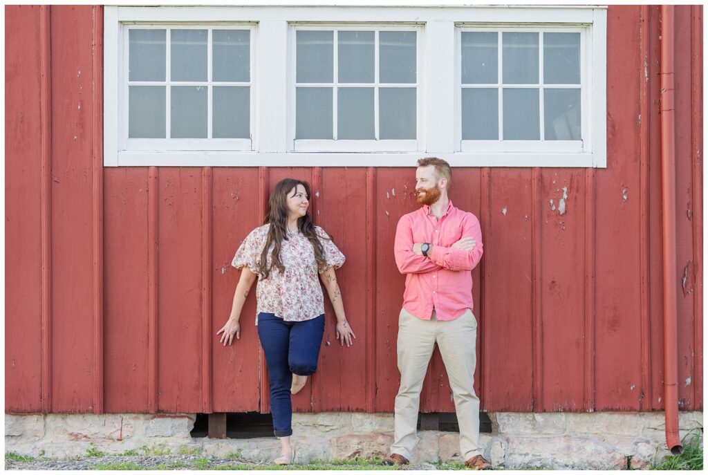 engaged couple leaning against a red barn wall outside in Lindsey, Ohio