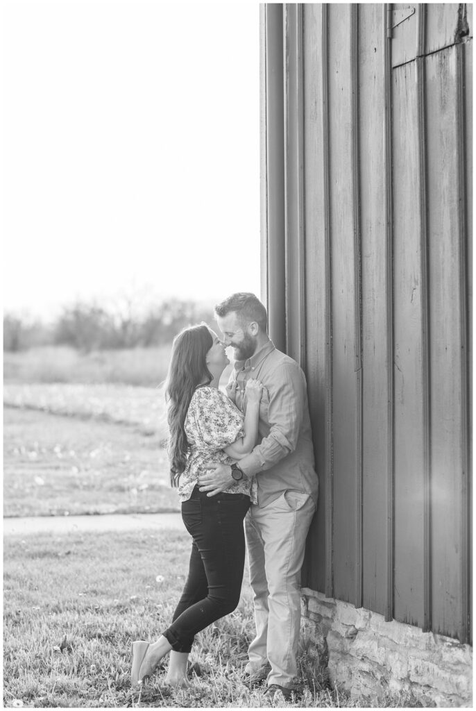 couple holding each other and leaning against a red barn at Creek Bend Farm