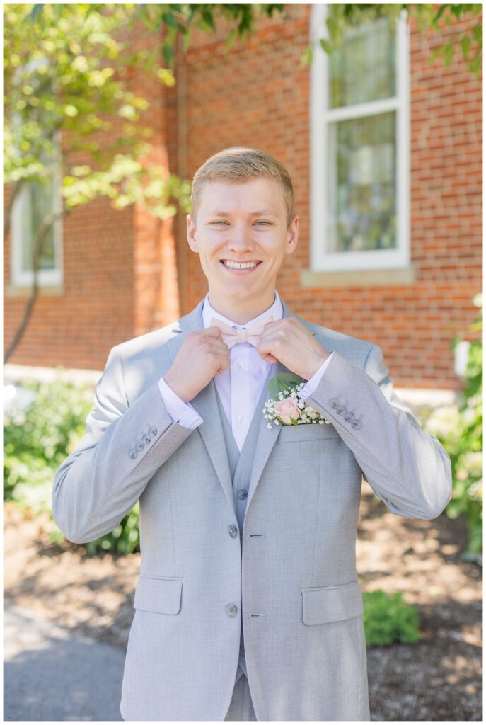 groom adjusting his bowtie in front of the brick church in West Mansfield, Ohio