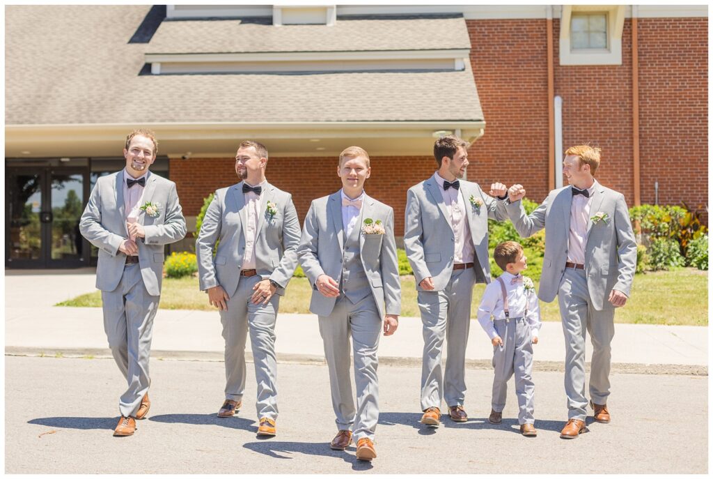 groomsmen and ring bearer walking with the groom outside the church in the sun