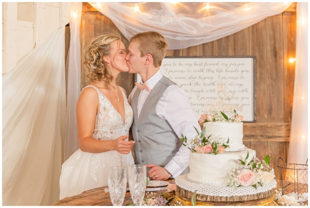 wedding couple share a kiss after cutting the cake together at Prairie Stone Farm venue reception