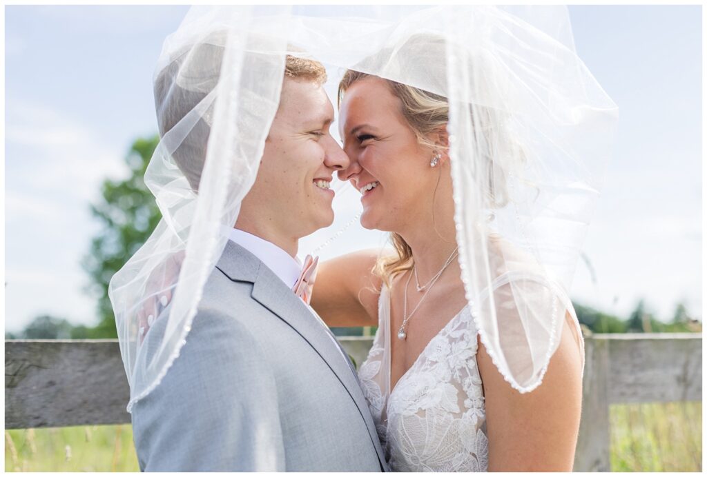 wedding couple standing underneath the bride's veil next to a wooden fence