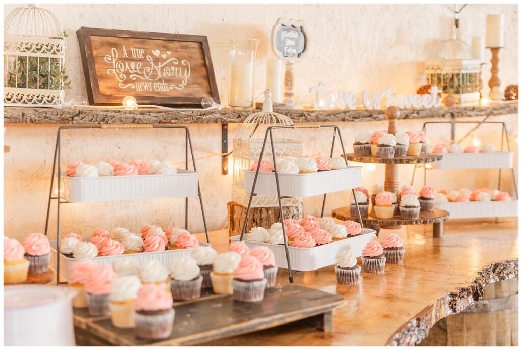 large wooden table with pink and white chocolate and vanilla cupcakes